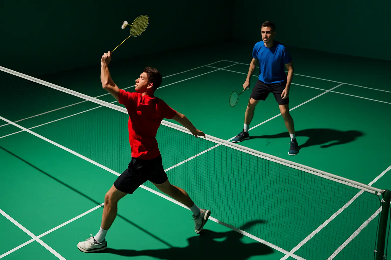 Malaysian badminton doubles players practicing on an indoor court with rackets raised